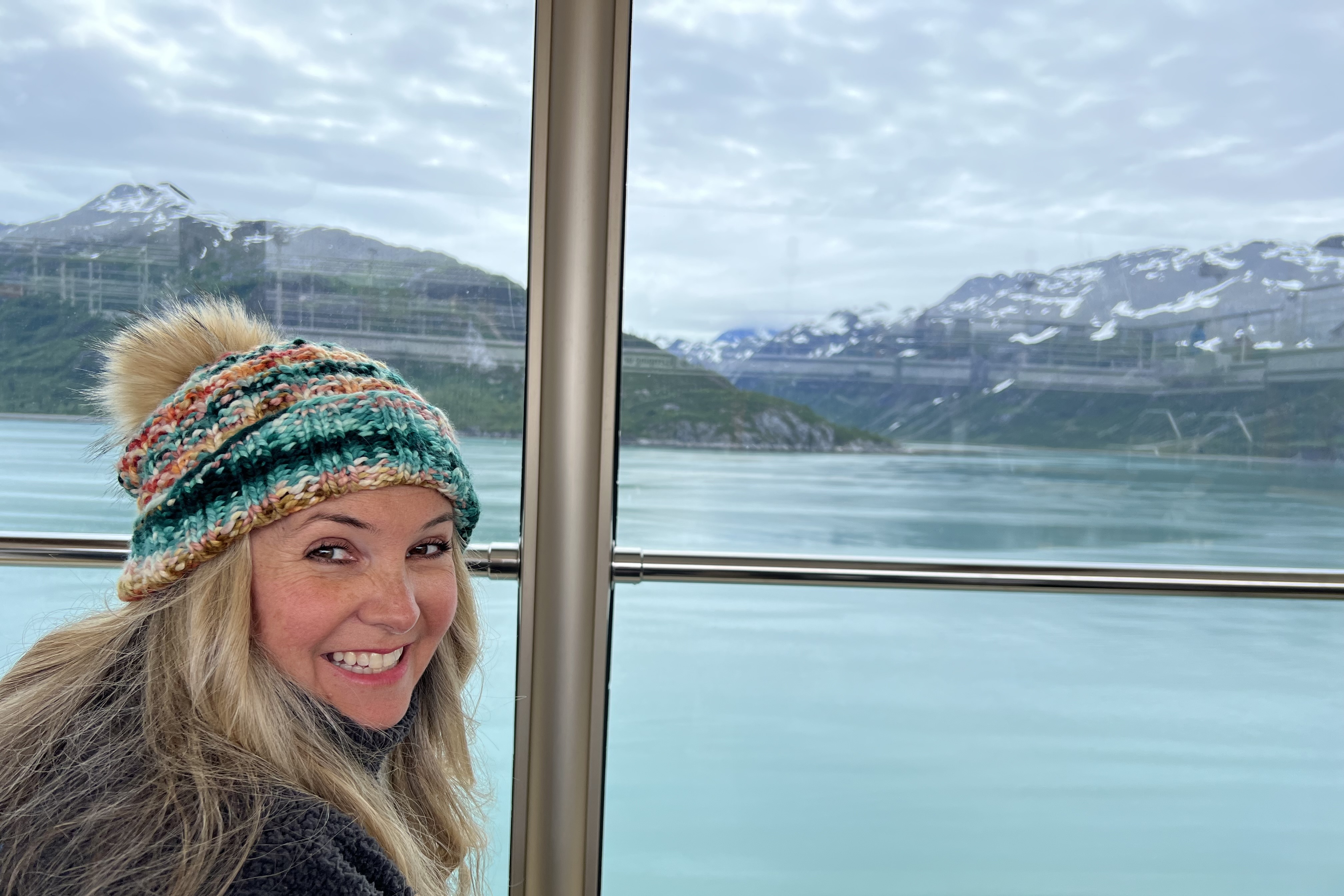 Angie in front of a window looking out on Mountains and water at Glacier Bay in Alaska