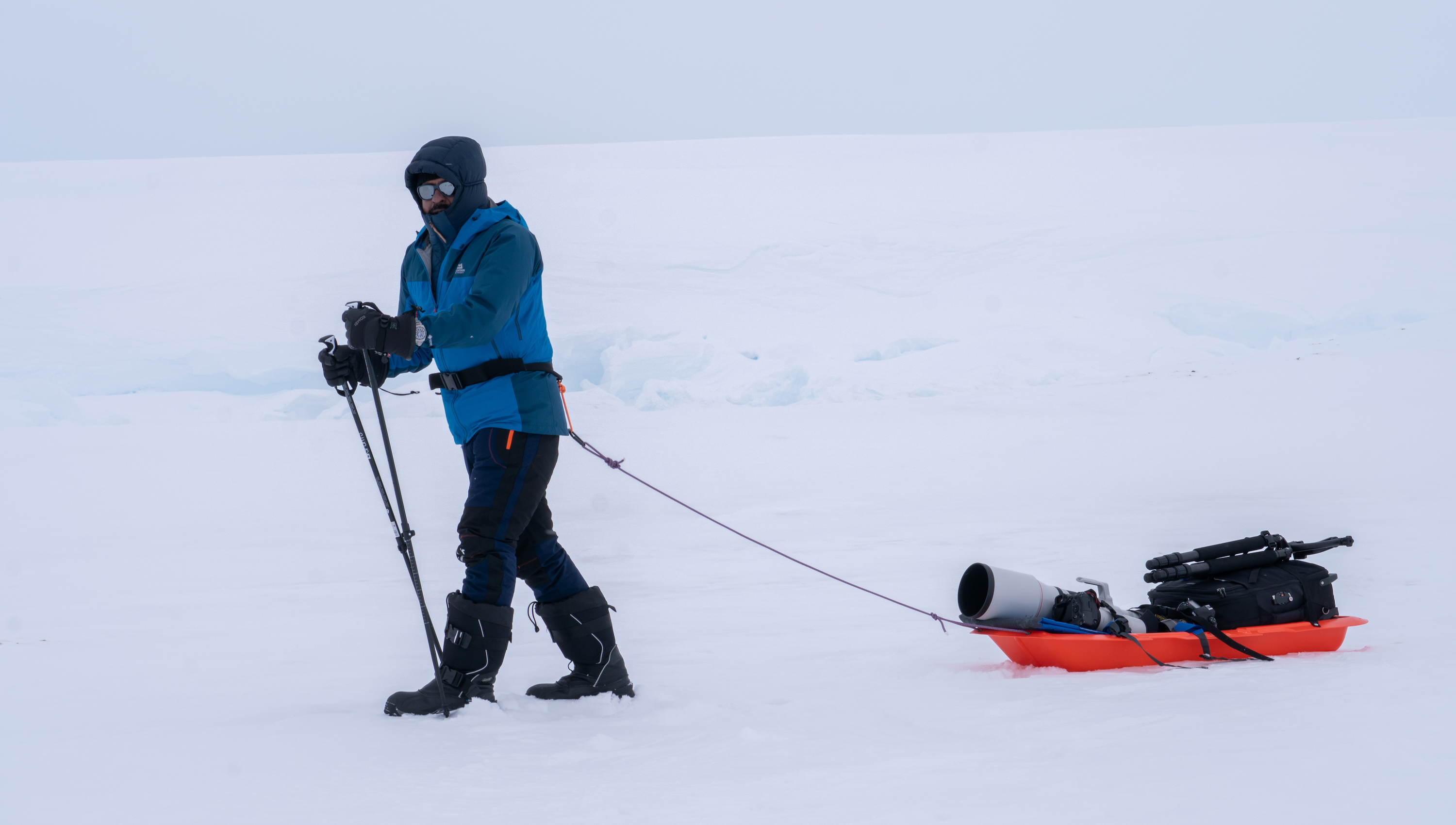 Photographer with sled and hiking poles in Antarctica, heading to an emperor penguin colony