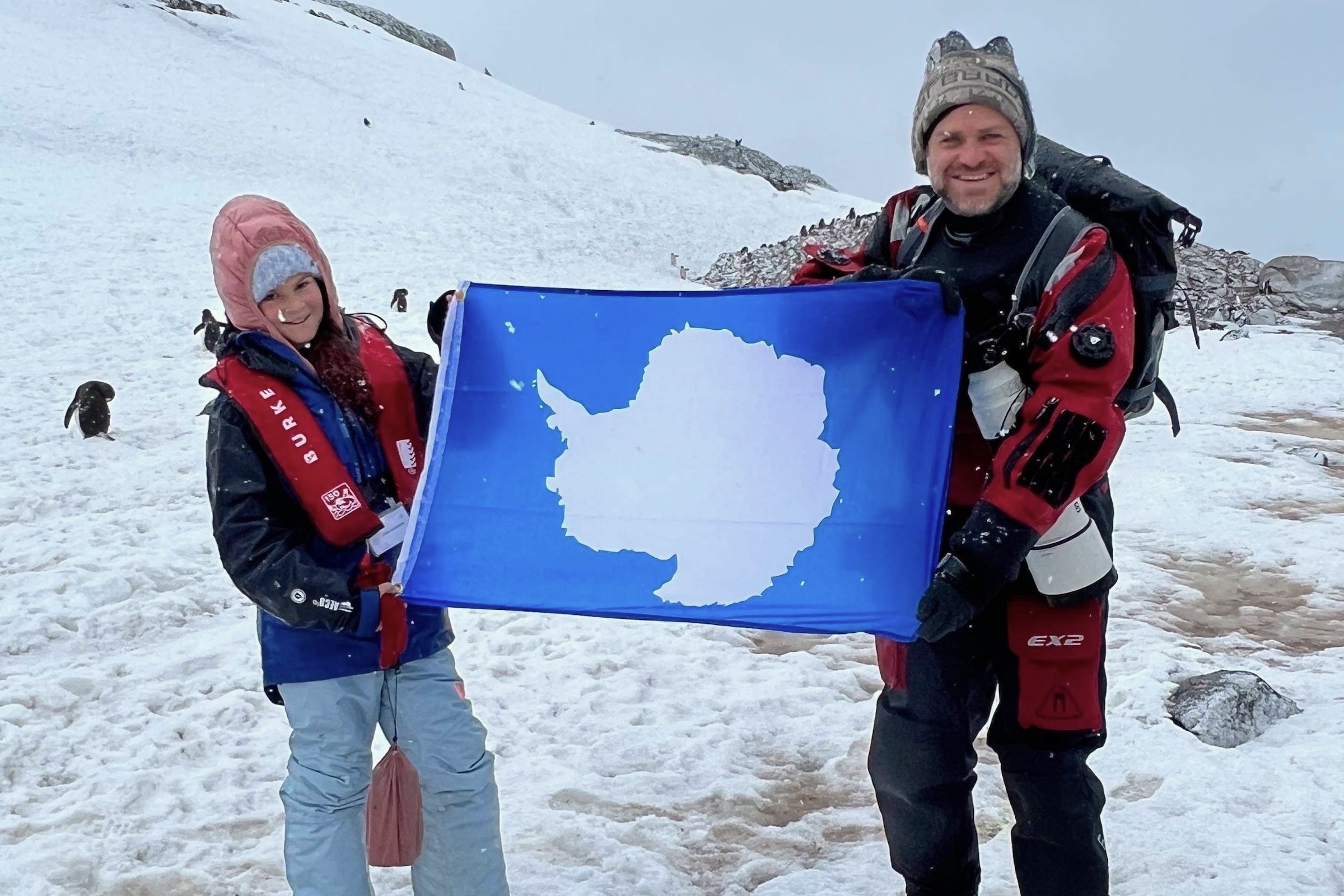 Father and daughter holding Antarctic flag in the snow