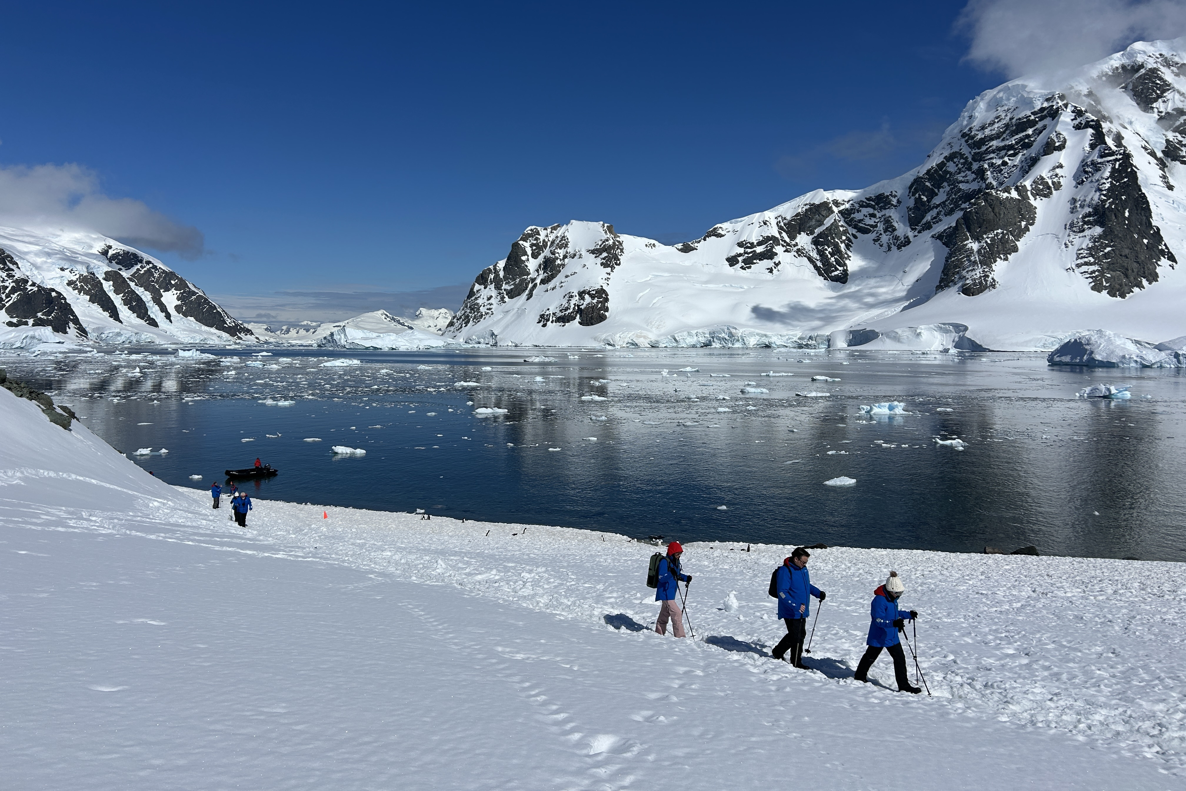 A small group of people walking to a penguin colony on Dako Island, mountain scenery and icy water