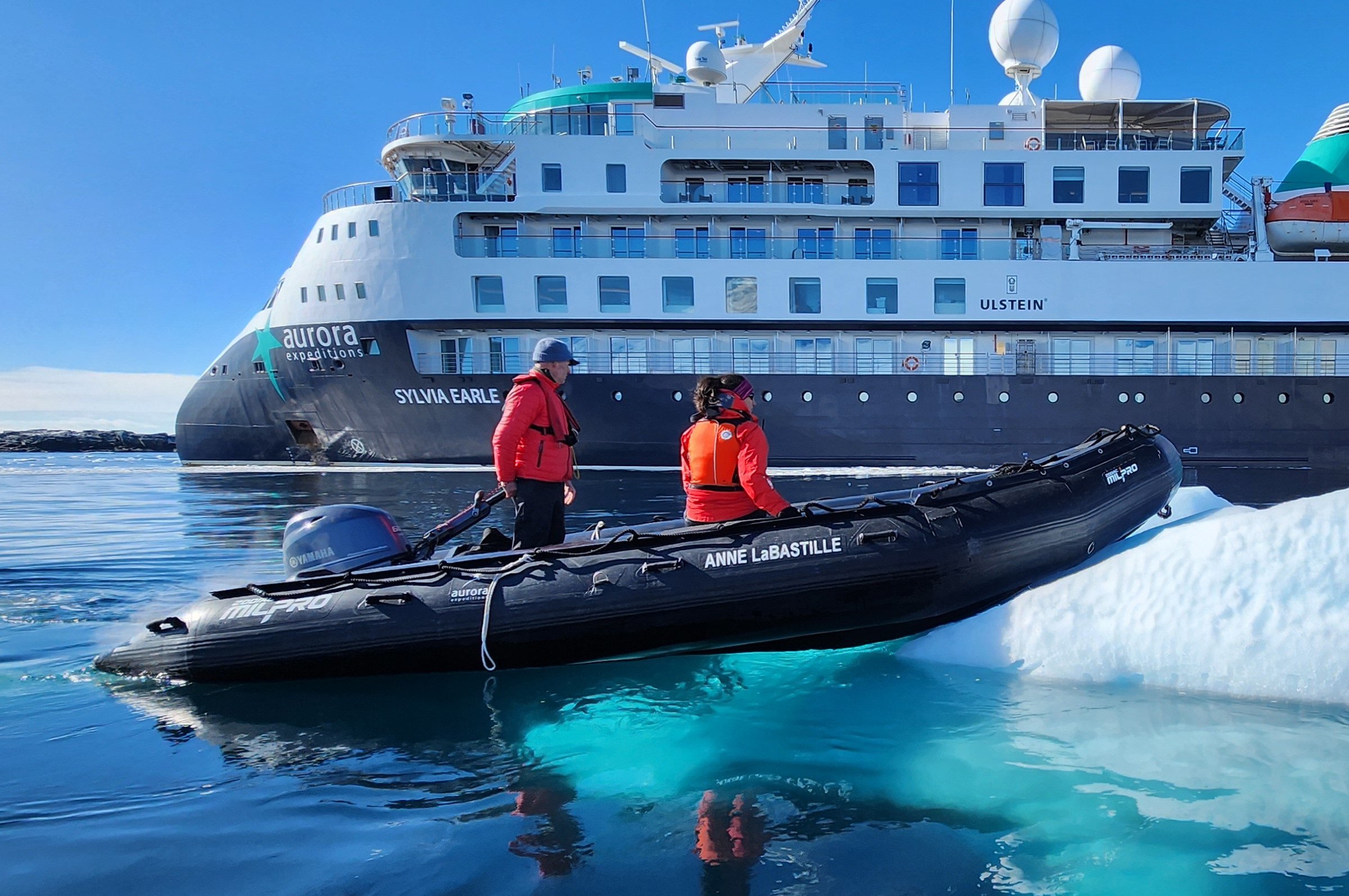 Zodiac parked on an ice floe in Antarctica, with the Sylvia Earle cruise ship in the background.