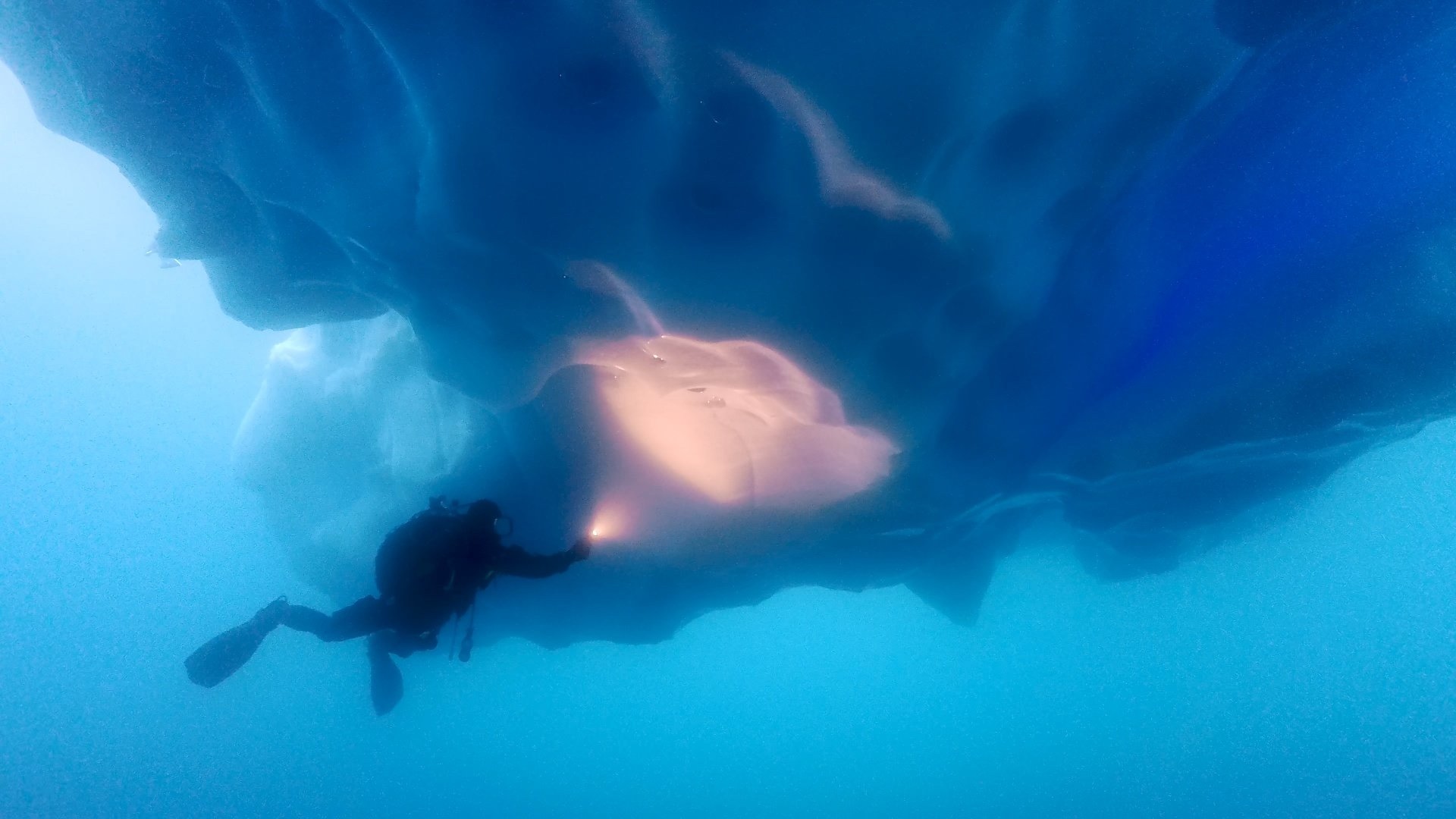 A scuba diver inspects the bottom of an iceberg in Antarctica