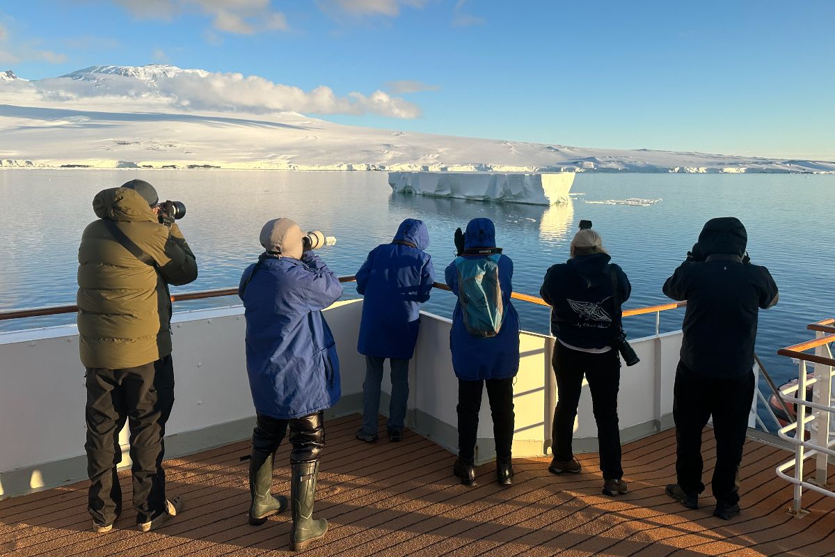 A group of Antarctic tourists stand on the deck of MS Adventurer in the Ross Sea photographing a tabular iceberg