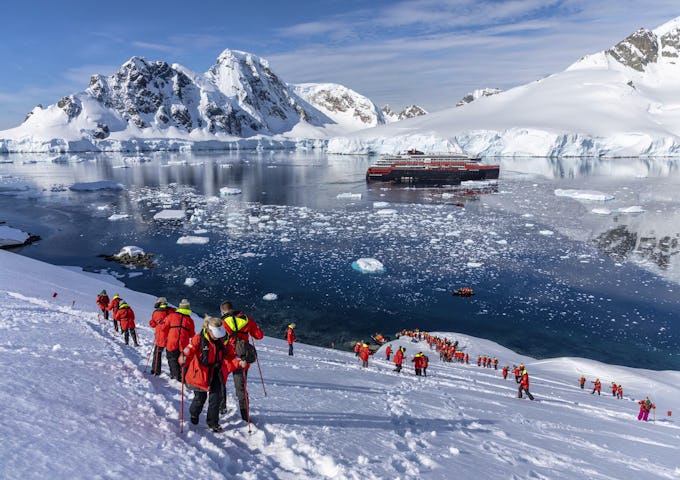 A group snowshoes in Orne Harbour, Antarctica, with a ship in the background