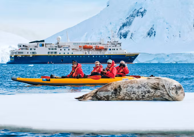 Guests kayak past a Weddell seal with the NG Explorer ship in the background