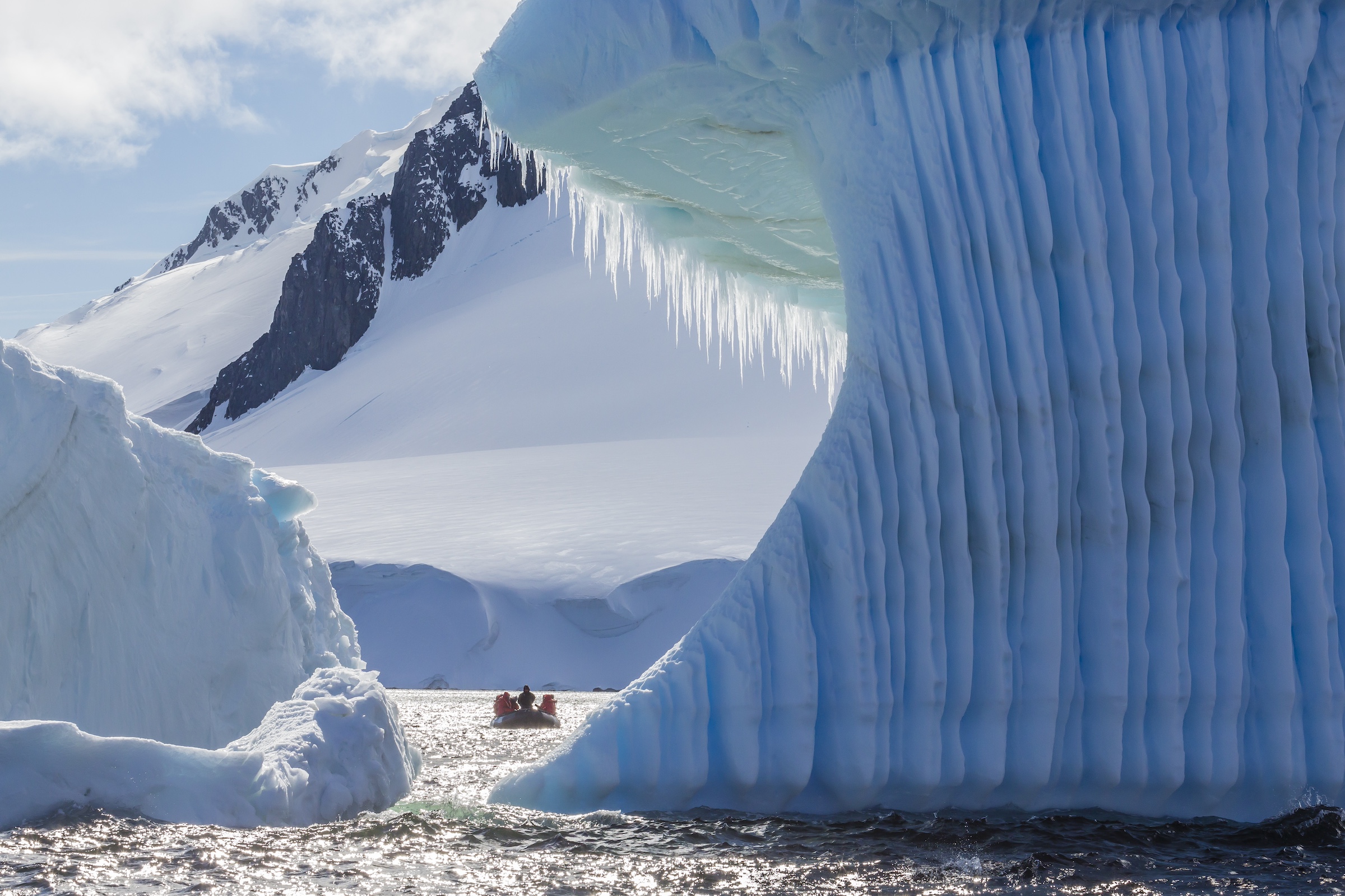 A zodiac boat cruises past an enormous wind-carved iceberg in Antarctica
