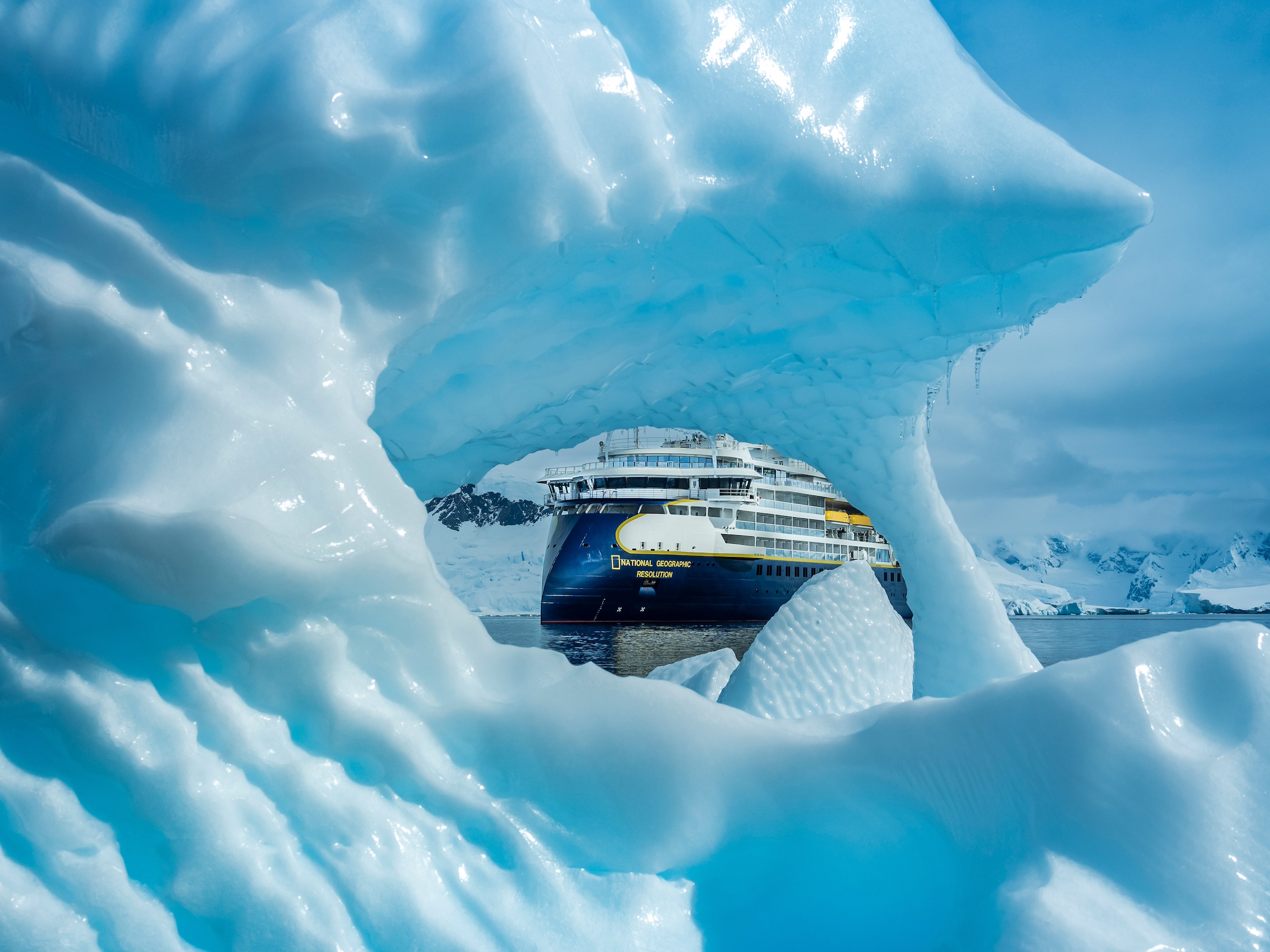 A ship is shown in the background through the hole of an iceberg in Antarctica 