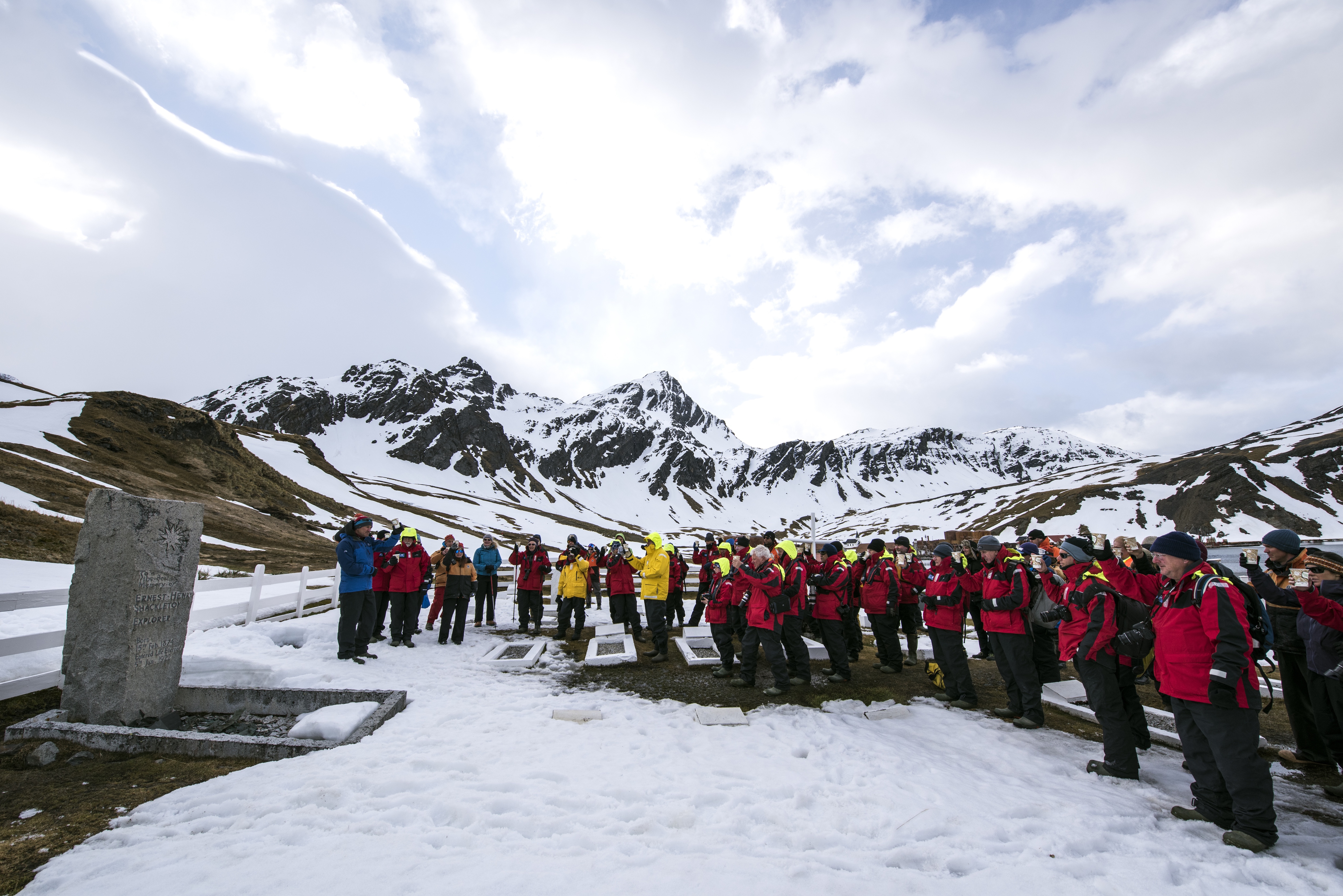 Tourists in red jackets stand in the snow around the grave of Sir Ernest Shackleton in Grytviken on South Georgia island
