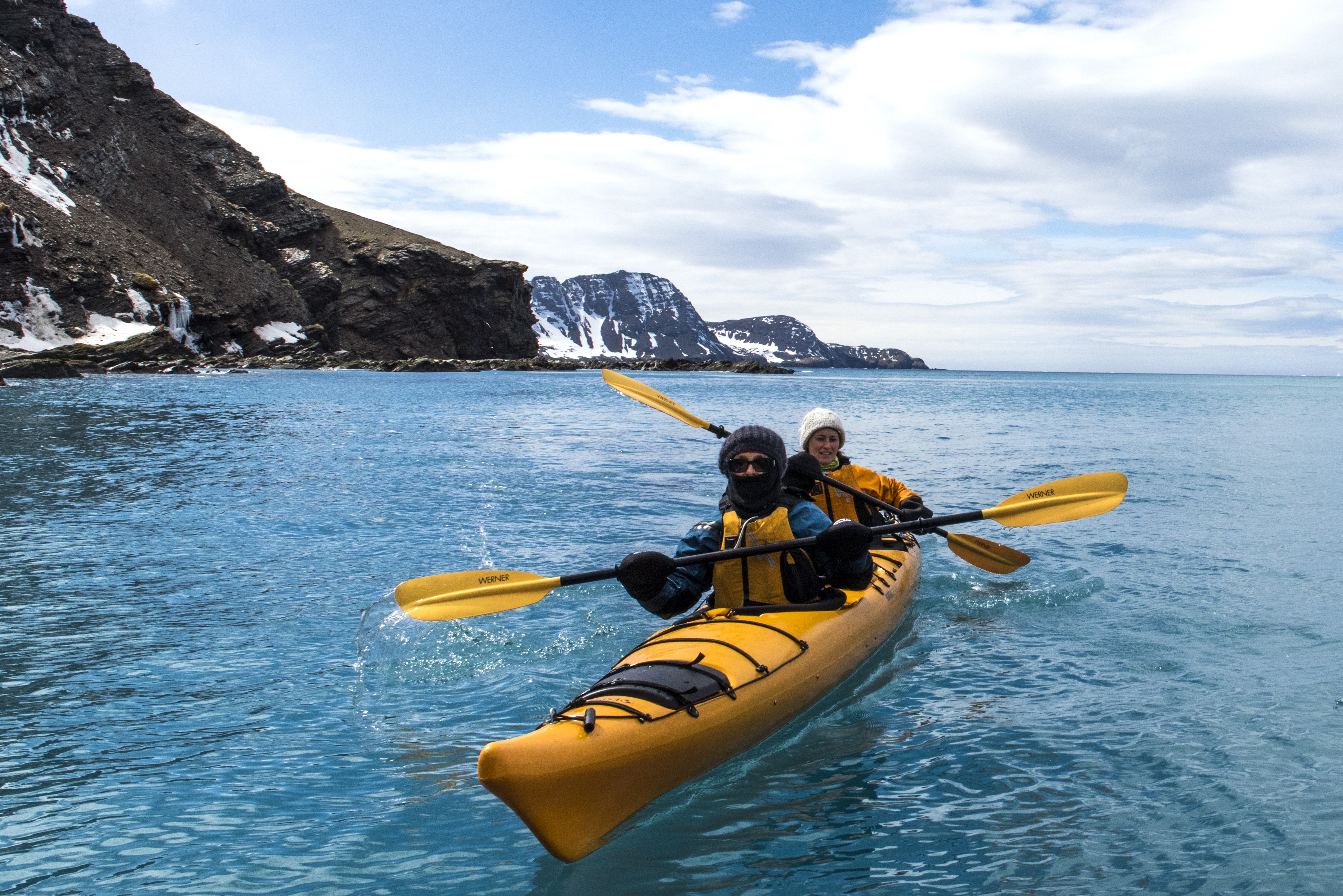 A yellow sea kayak with two people paddles on a calm bay in Jason Harbour, South Ger