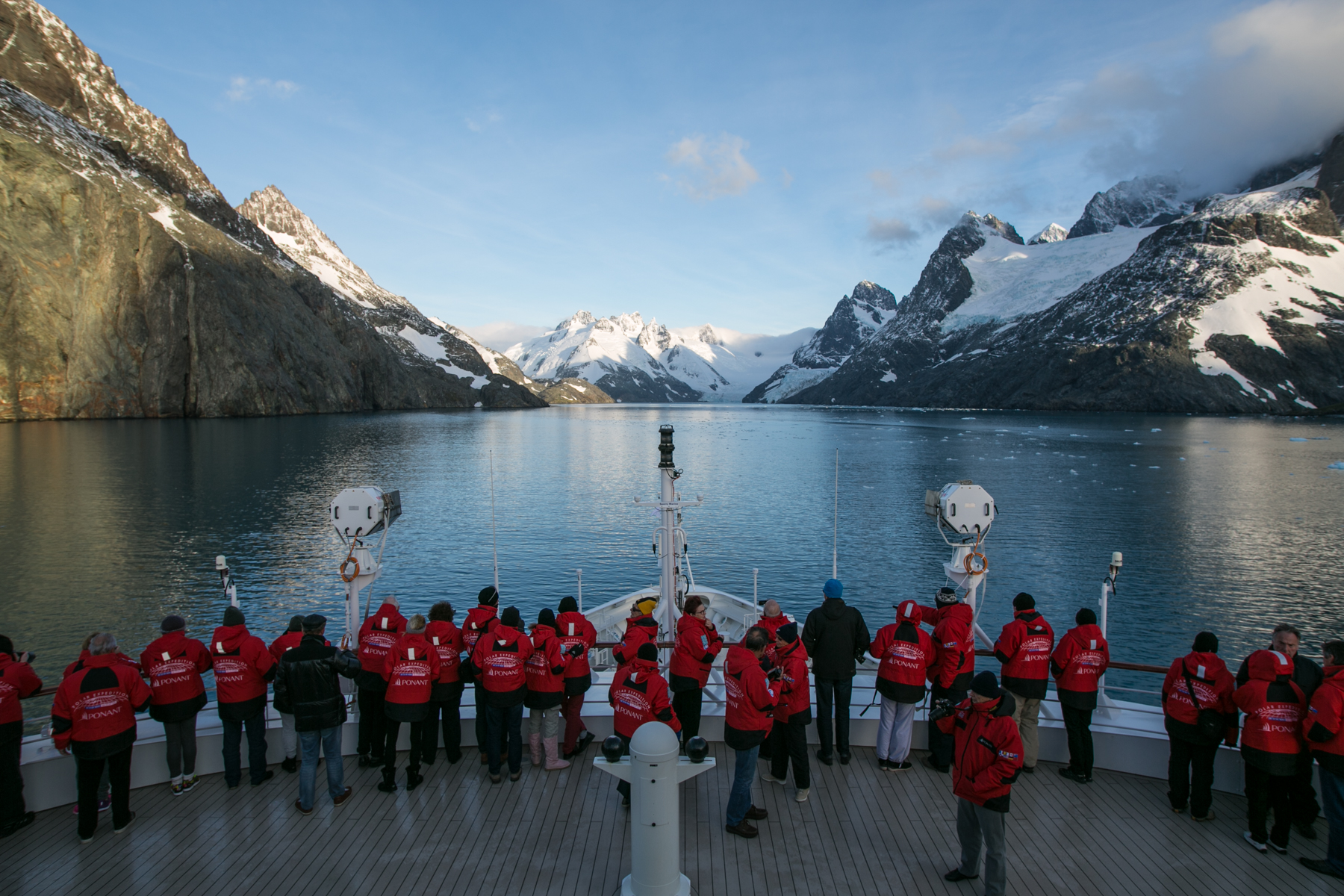 Passengers looking over the bow of an expedition cruise ship looking at the glaciers and mountains at the head of Dryglaski Fjord, South Georgia