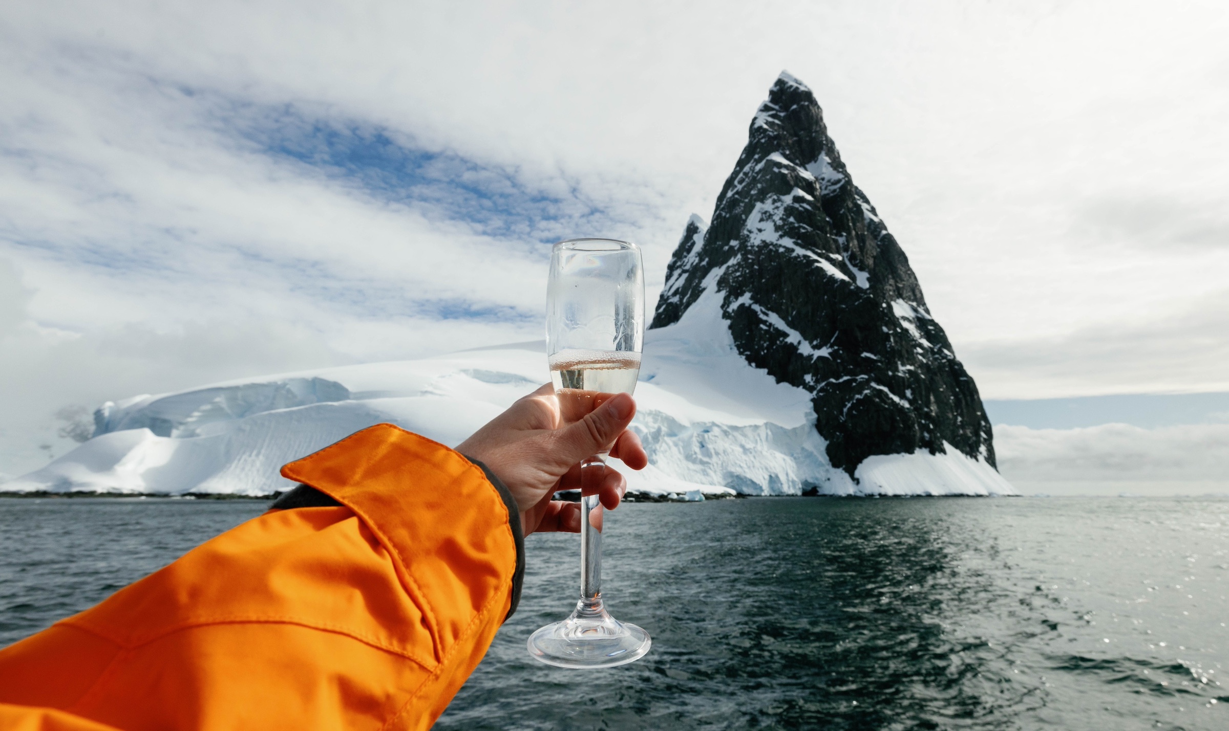 A hand holds up a Champagne glass in front of an Antarctic island