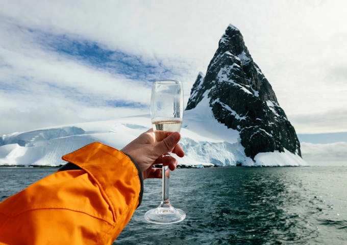 A hand holds up a Champagne glass in front of an Antarctic island