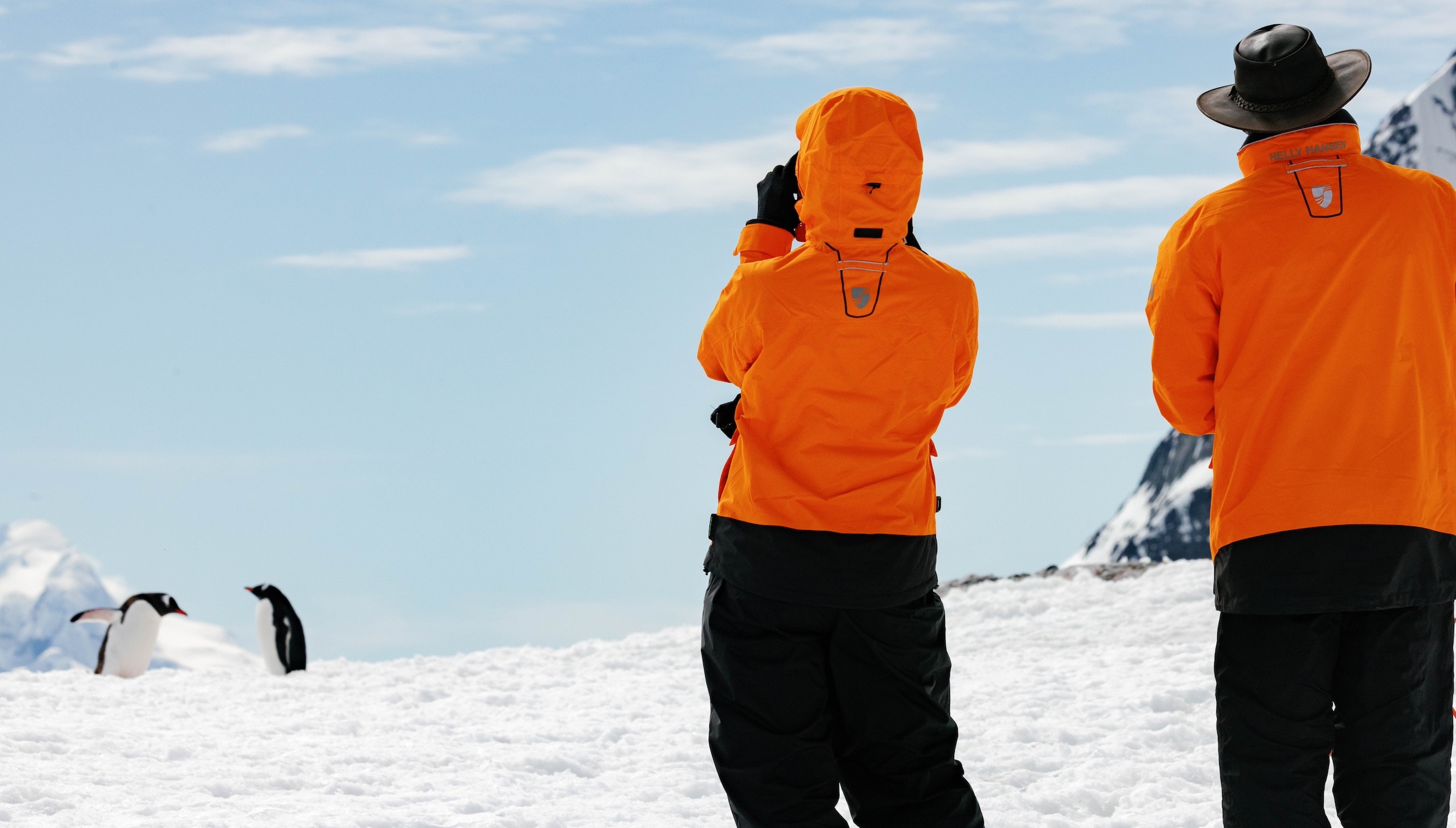 Two people explore take a picture of a penguin as they explore Booth Island, Antarctica 