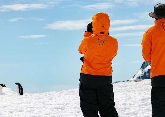 Two people explore take a picture of a penguin as they explore Booth Island, Antarctica