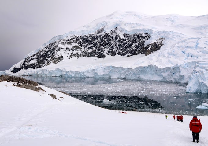 Guests on an Antarctic cruise trudge down a snowy slope towards the bright blue sea
