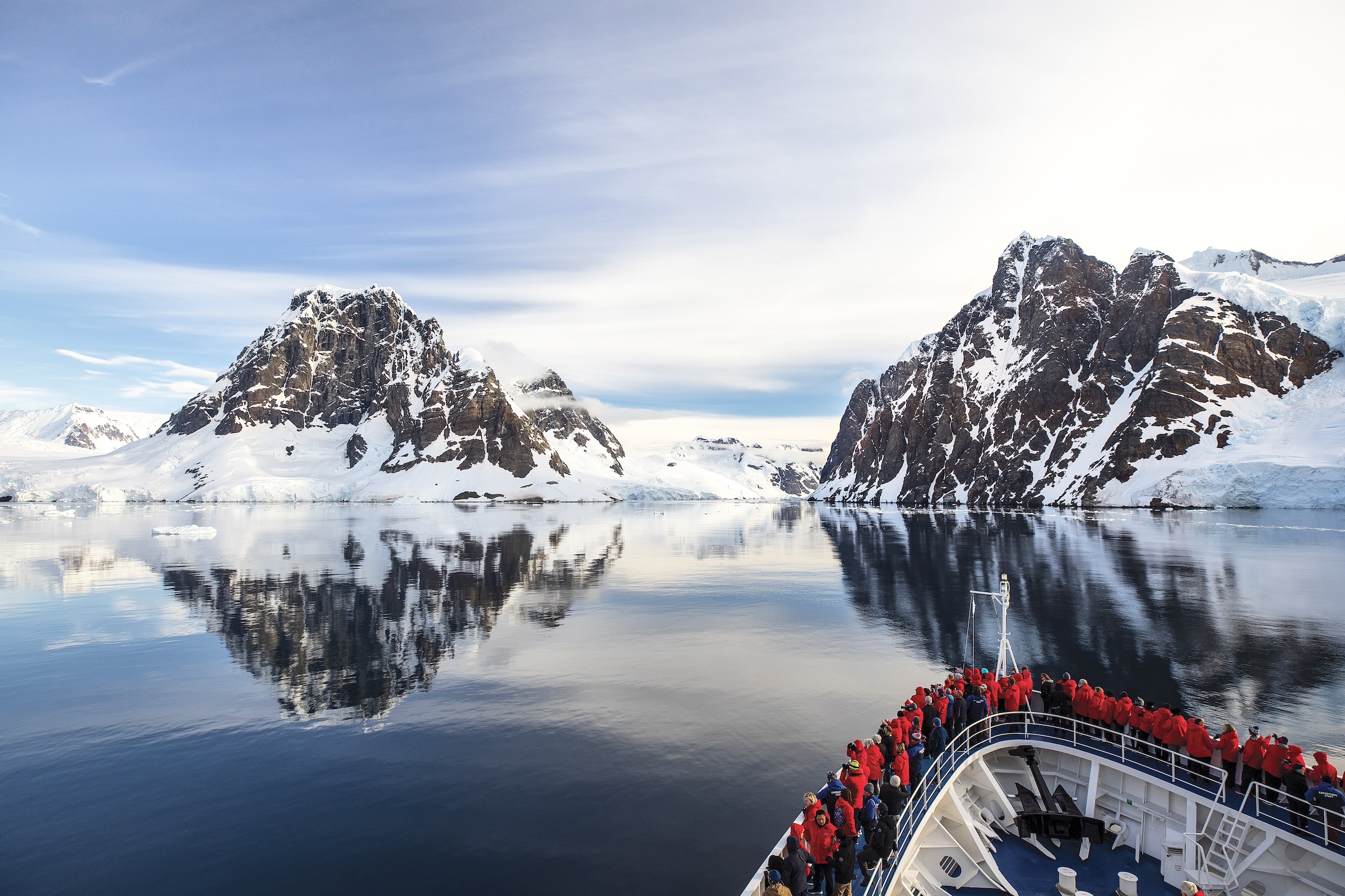 The bow of a ship is shown sailing through the glassy sea of the Lemaire Channel