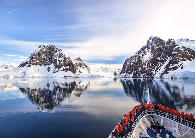 The bow of a ship is shown sailing through the glassy sea of the Lemaire Channel