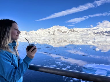 A woman looks out across to Antarctic scenery from a ship with a cup of maté tea in hand