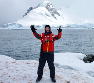 Colin, a Swoop sales team member, holds up his hands to signify the number seven as he stand in an Antarctic landscape