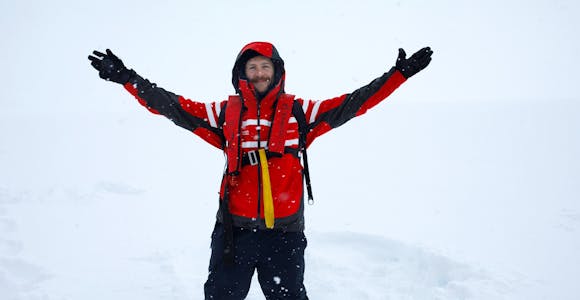 Colin from Swoop holds his hands up to the sky as if embracing the snow in Antarctica