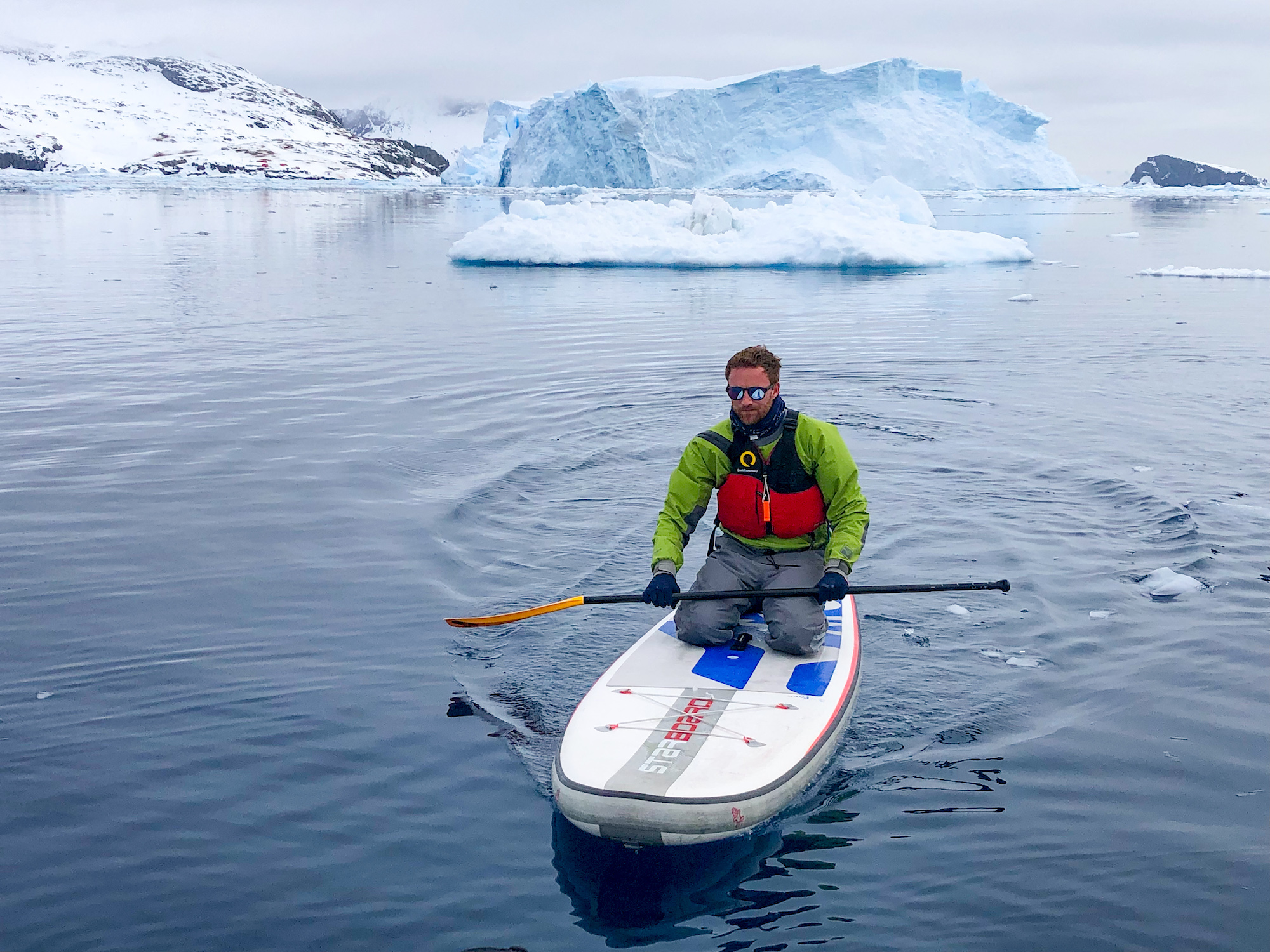 A man kneels while paddleboarding in Antarctica 
