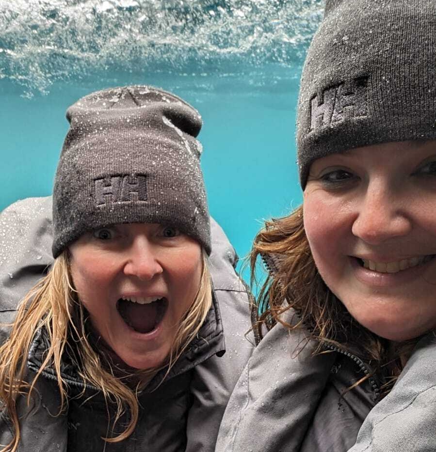 Two women look ecstatic as they explore underwater in Antarctica in a submarine