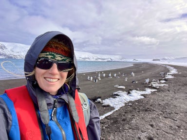A woman stands on Deception Island, Antarctica, with penguins in the background
