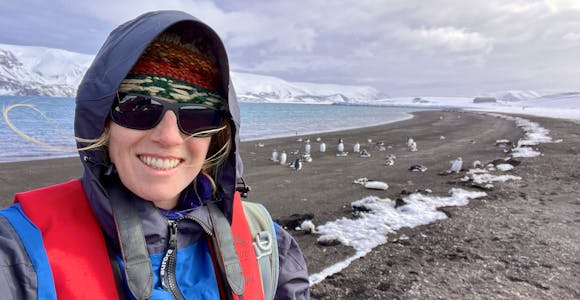 A woman stands on Deception Island, Antarctica, with penguins in the background