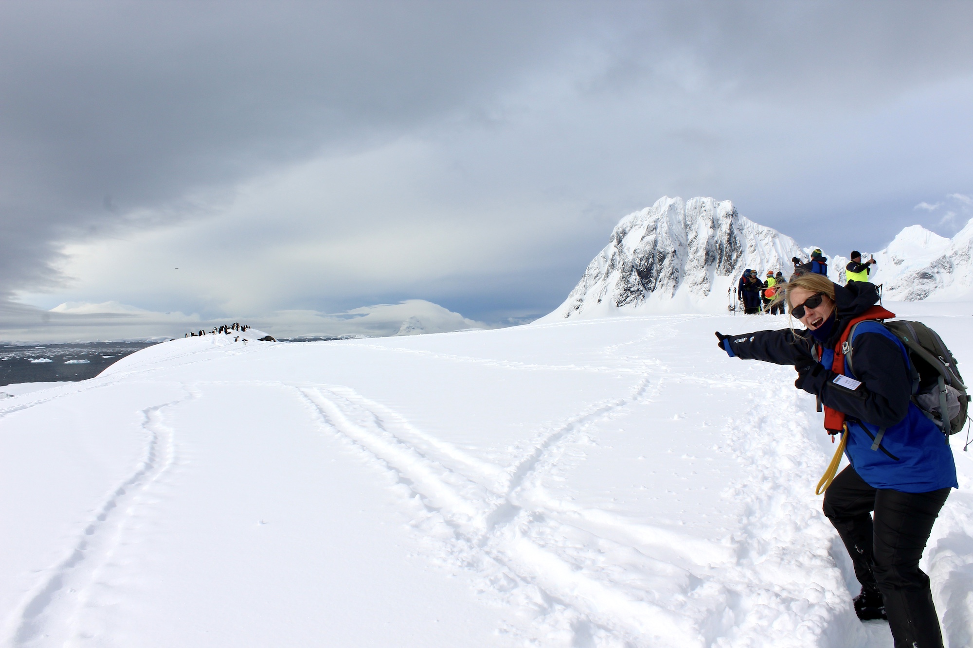 A woman points excitedly to a group of penguins in the background in Antarctica