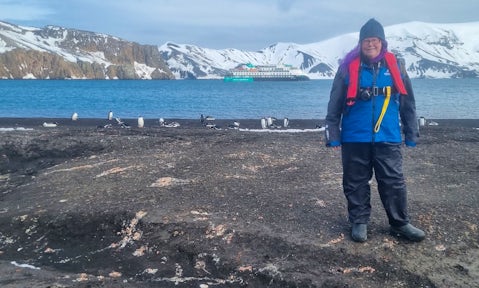 A woman poses in front of a ship on Deception Island, Antarctica