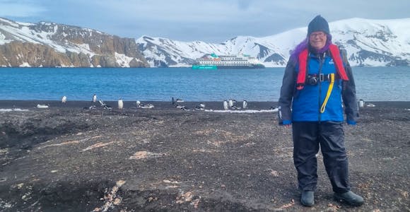 A woman poses in front of a ship on Deception Island, Antarctica