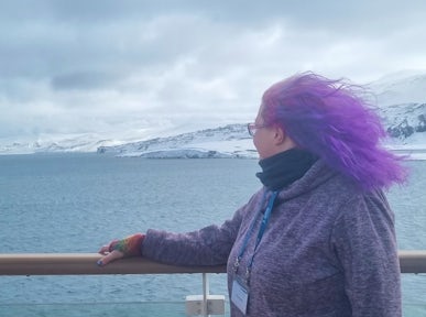 A woman stands on a ship and looks out at Deception Island in Antarctica