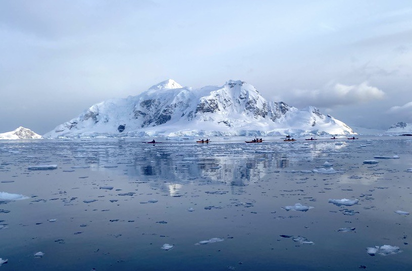 Kayakers in the distance in front of a classic Antarctic scene
