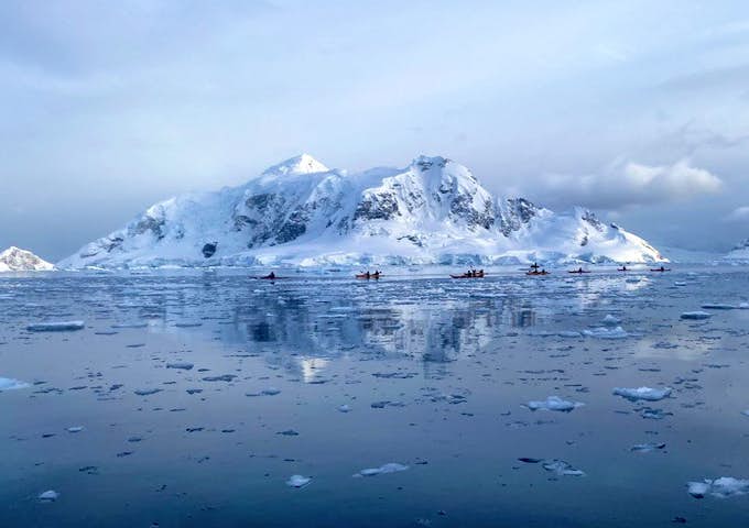 Kayakers in the distance in front of a classic Antarctic scene
