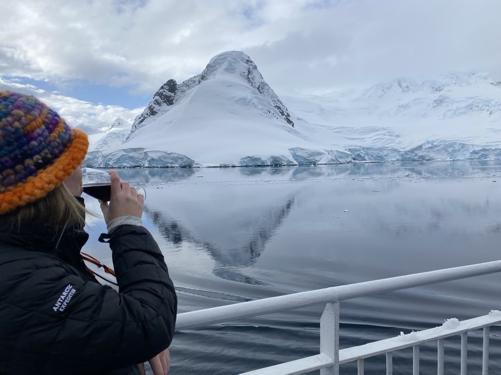 A woman drinks red wine while looking out onto a view of Antarctica 