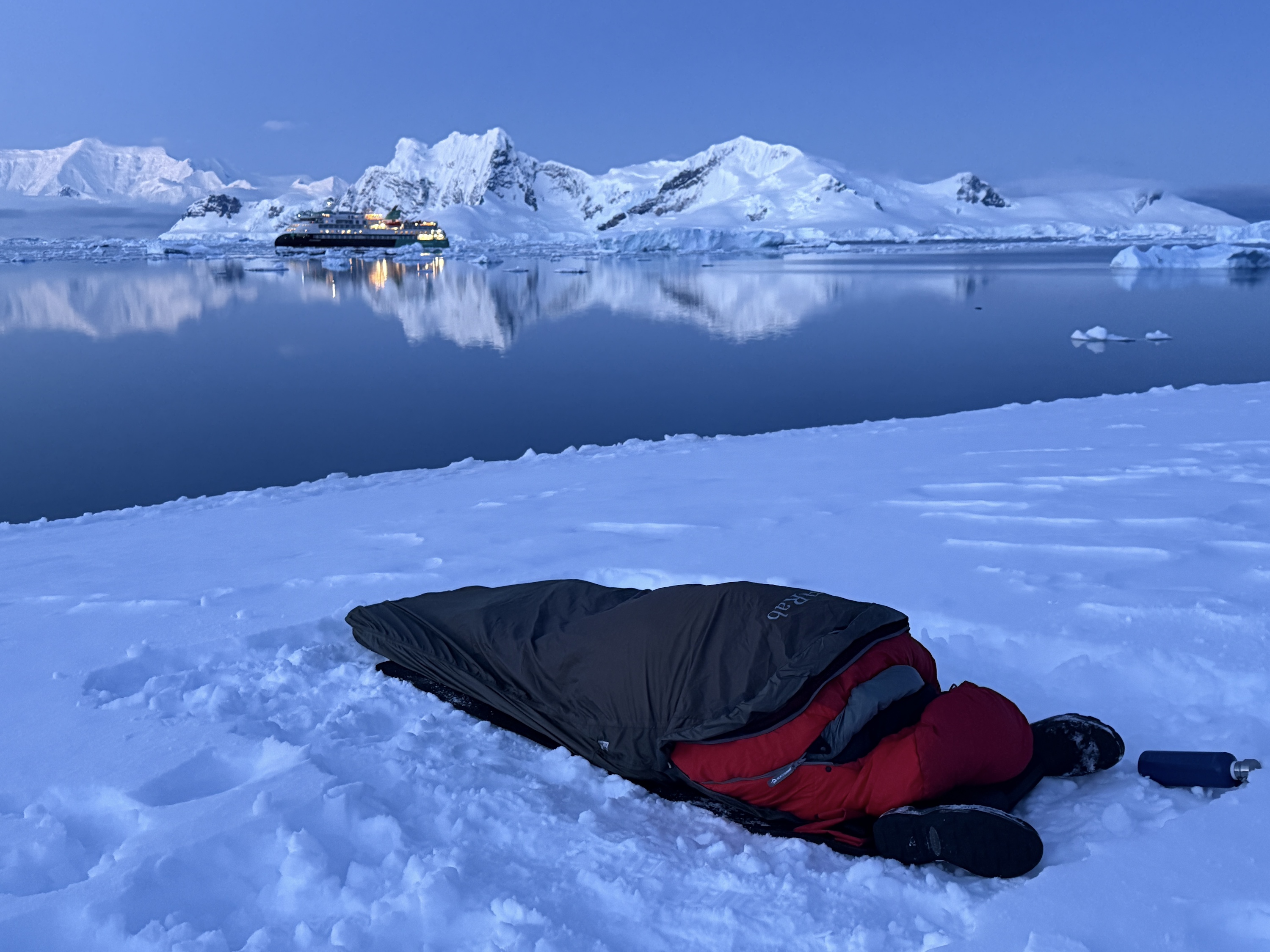 A sleeping bag lies on the ground in front of an Antarctic bay at dusk 