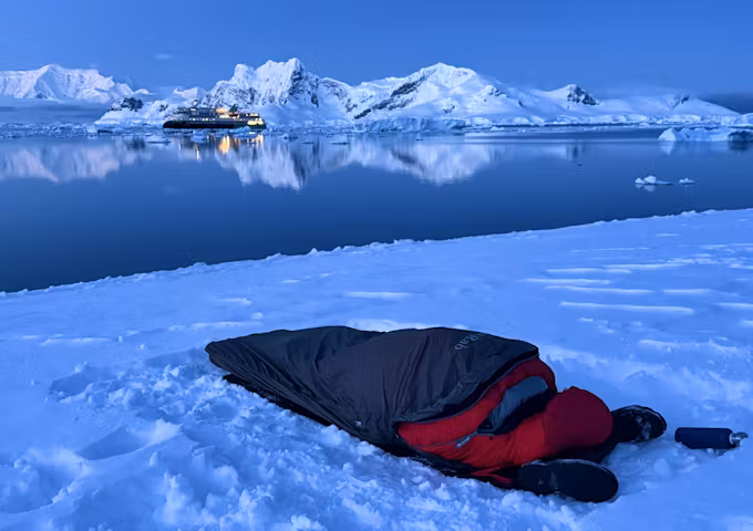A sleeping bag lies on the ground in front of an Antarctic bay at dusk