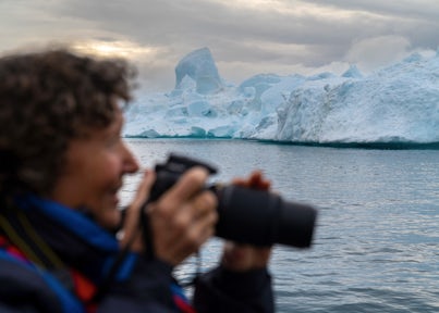 Photographer raising her camera to take a shot of an iceberg