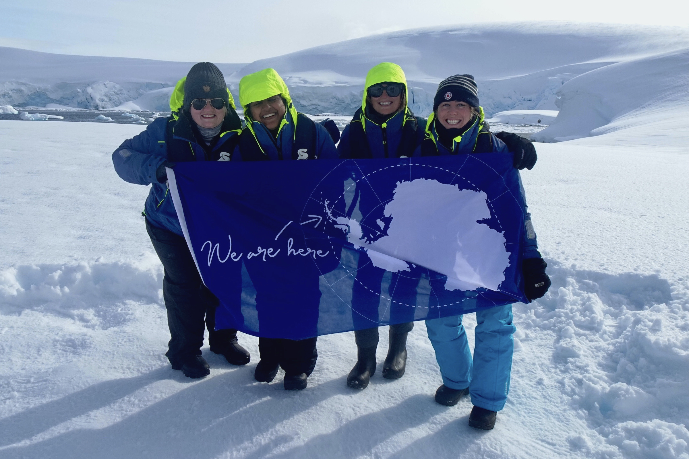 Four toursits in the snow hold an Antarctic flag to celebrate reaching the 7th Continent