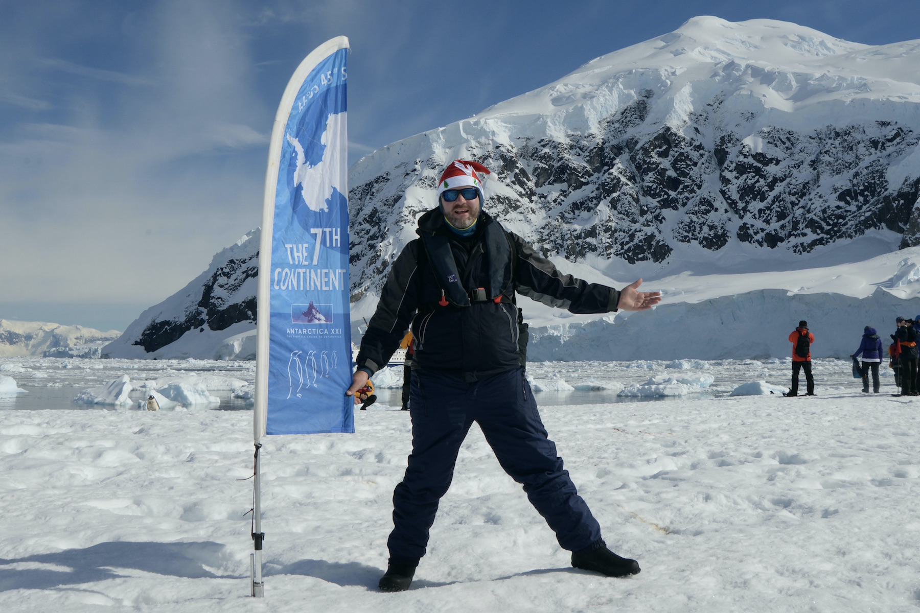 A man standung next to a 7th Continent flag in Antarctica
