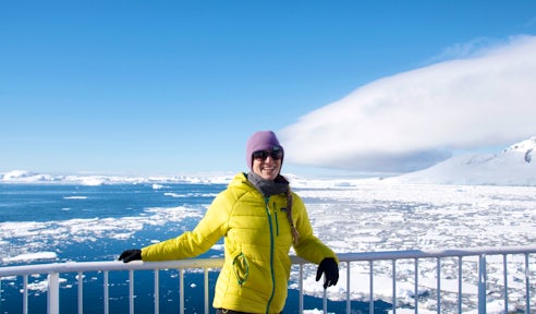 A woman stands on the deck of a ship with Antarctica in the background