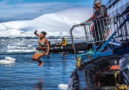 A woman jumps into the freezing polar waters while attached to a rope in Antarctica