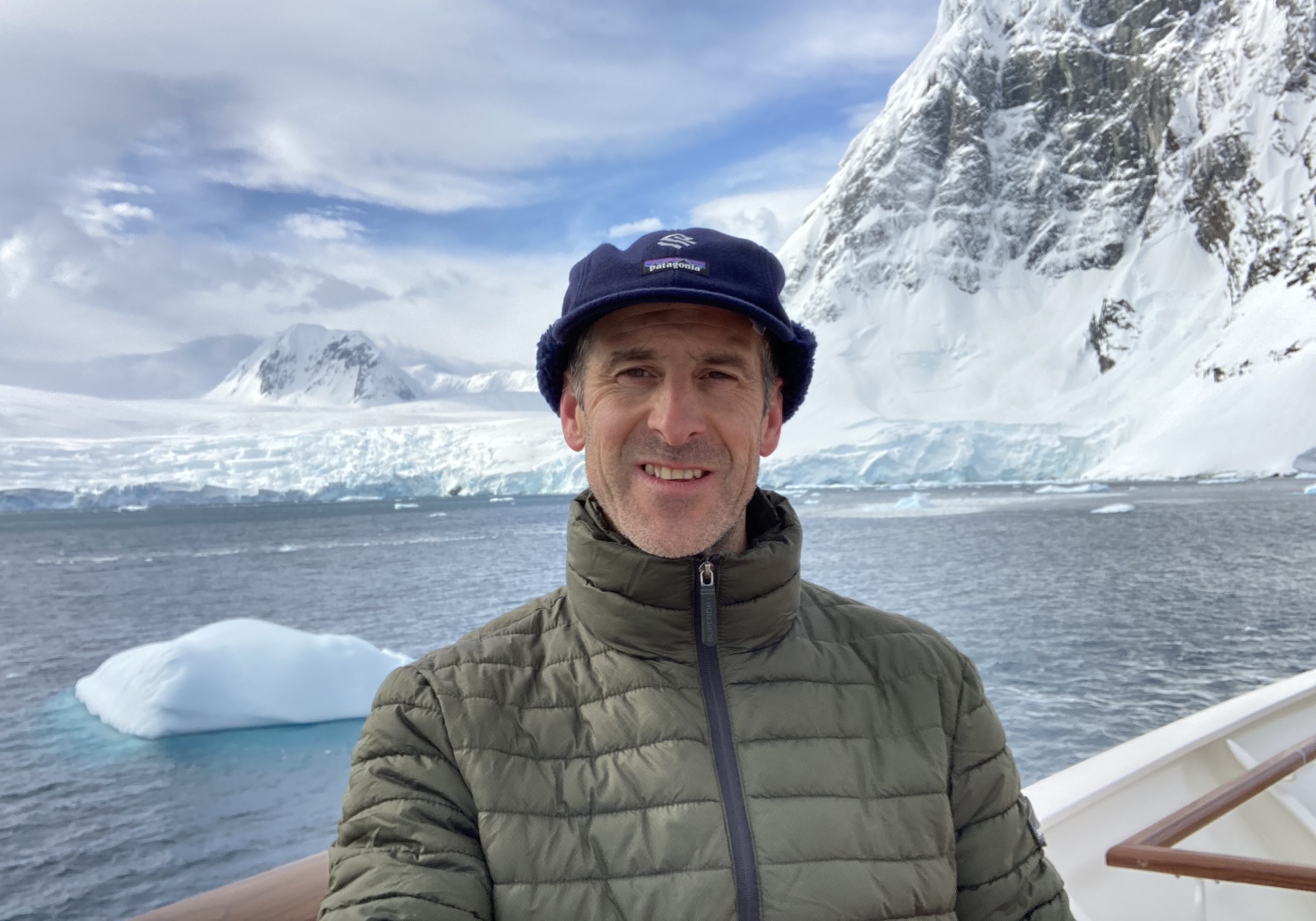 A man stands on a boat and smiles in Antarctica 