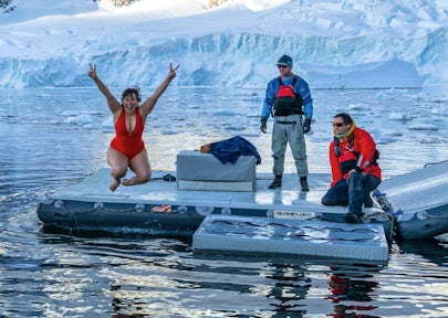 Carys from Swoop holds up her fingers in a V for Victory shape and does the polar plunge in Antarctica