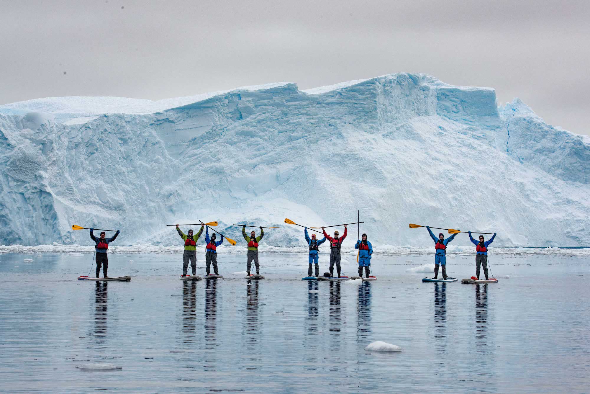 A group of paddleboarders raise their paddles as they paddleboard in Antarctica