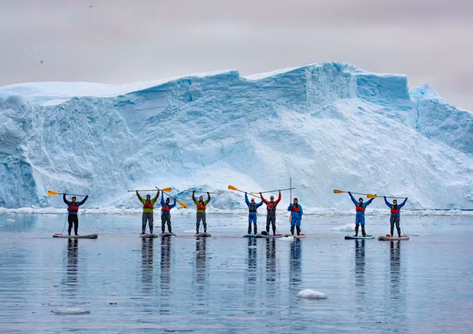 A group of paddleboarders raise their paddles as they paddleboard in Antarctica