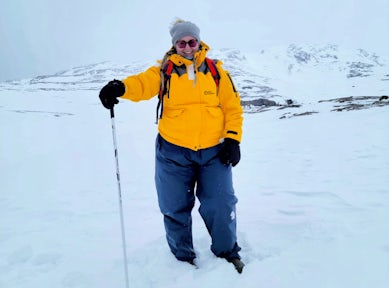 A woman holds a hiking pole and poses in front of a snowy backdrop