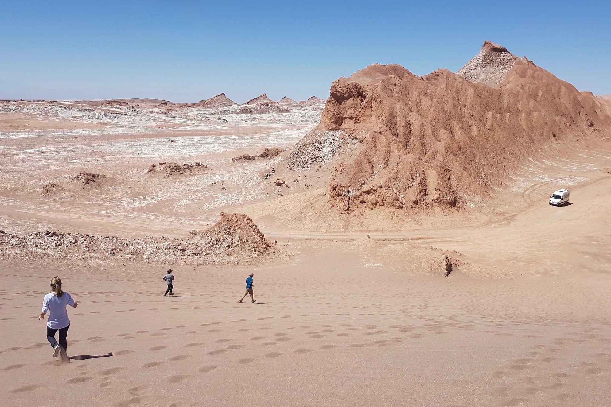 Tiny figures of hikers explore the vast red sandy rocks of Vallecito in Chile's Atacama Desert