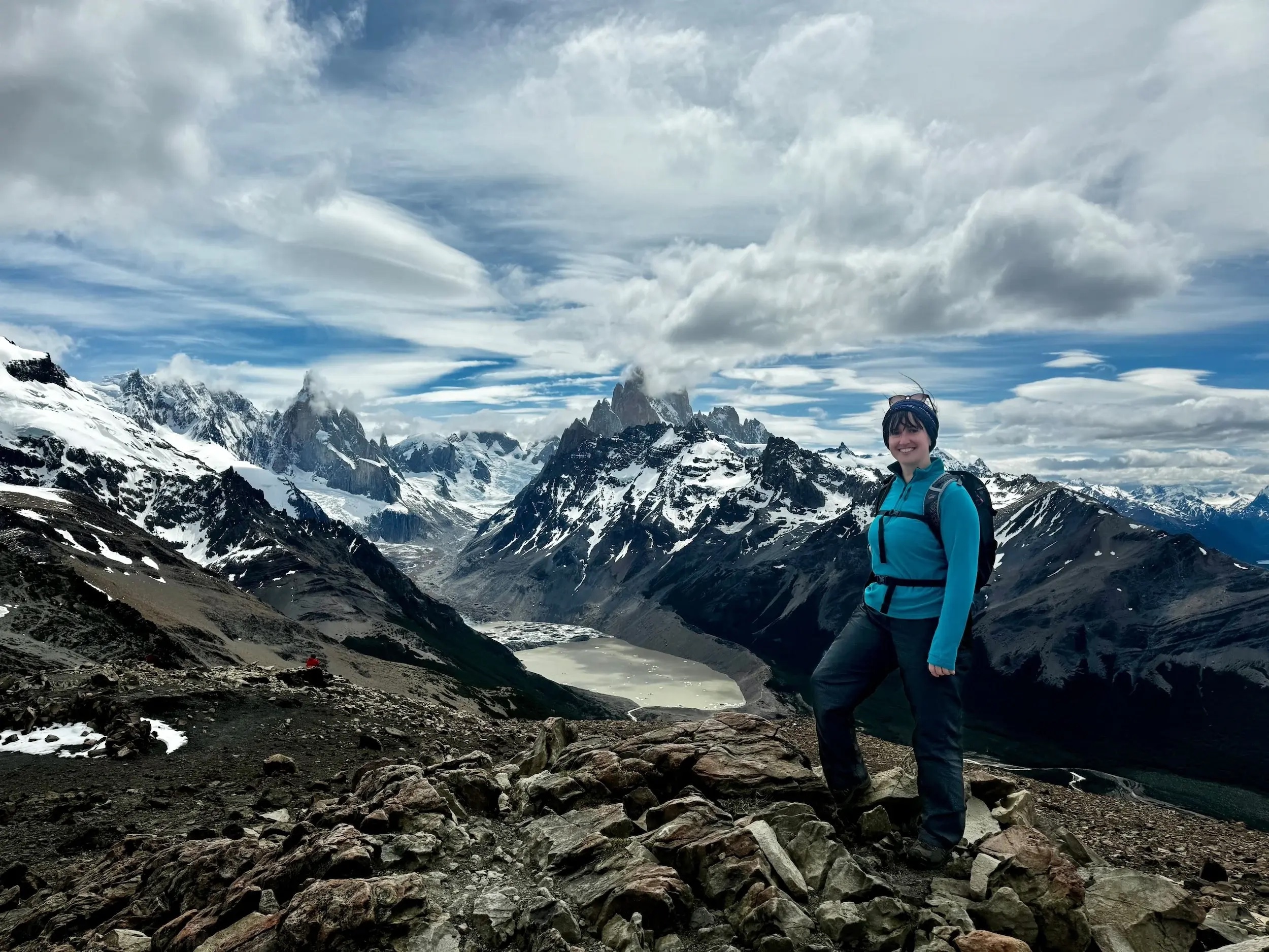Carys from Swoop poses on top of a mountain with snowy peaks and a lake in the backdrop at El Chalten
