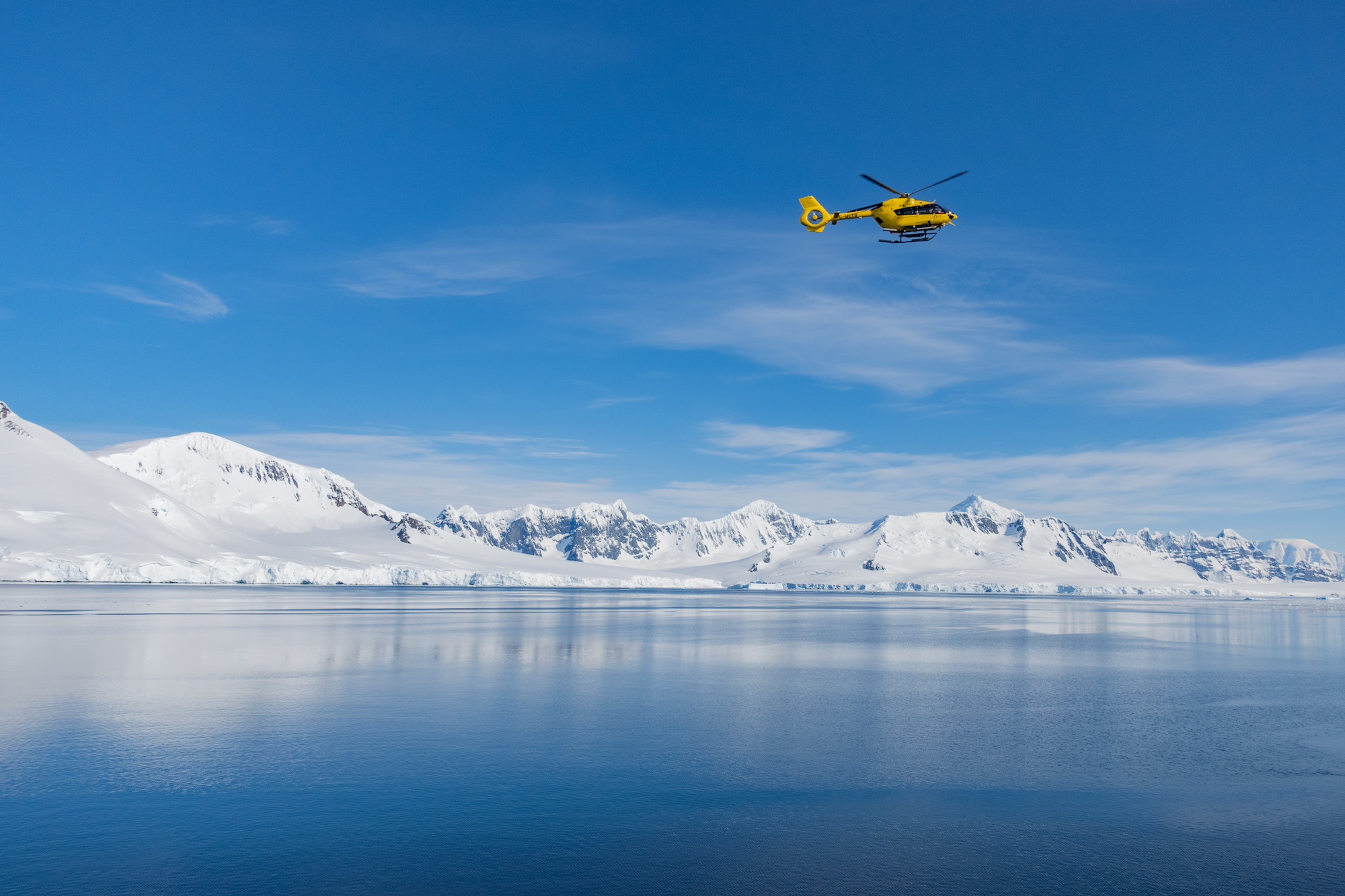 A helicopter flies through the blue Antarctic skies